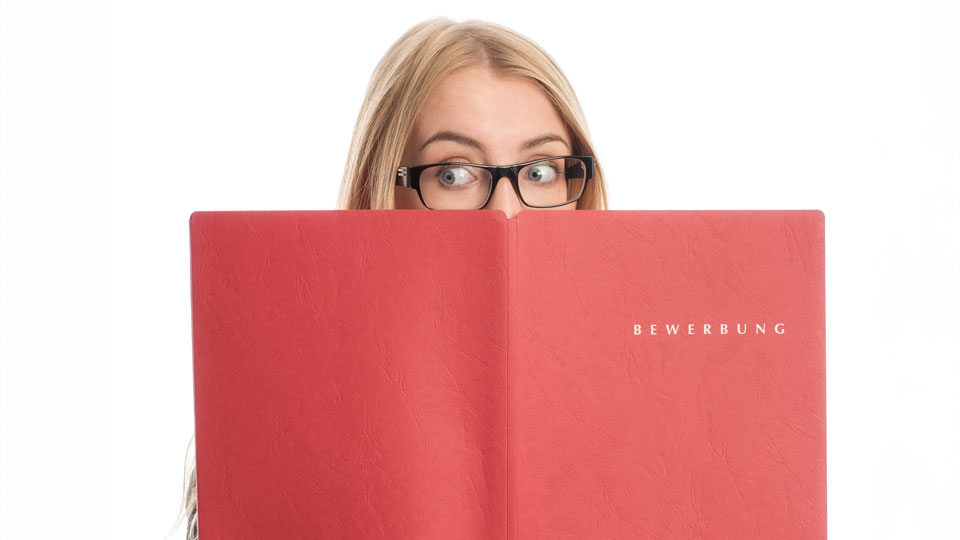 Auf dem Bild ist eine Frau die über ein Bewerbungsheft drüber schaut