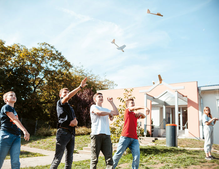 Schulkinder sind zusammen draußen und werfen kleine Holzflieger in die Luft