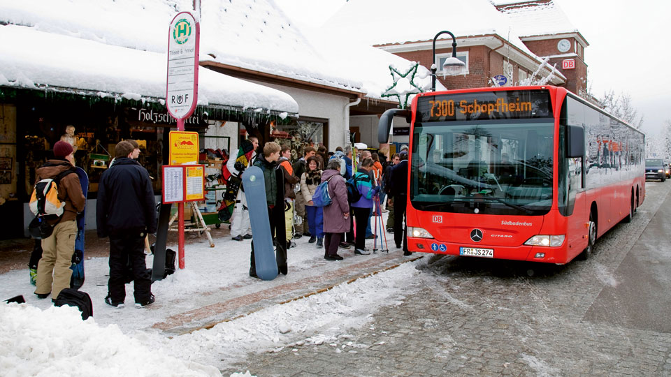 Personen stehen an einer Bushaltestelle und steigen in einen Bus.
