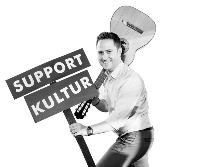 Ein Bild von einem Mann der ein Schild hebt mit dem Text "Support Kultur" darauf