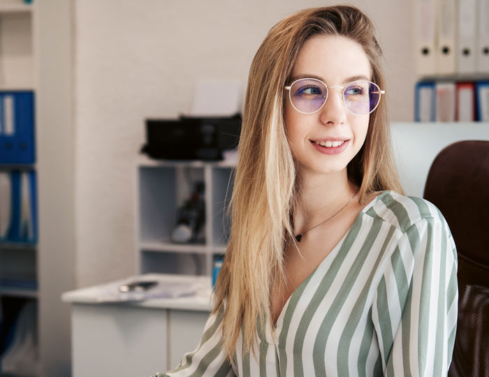Auf dem Bild ist eine Frau die in einem Büro sitzt und lächelt.