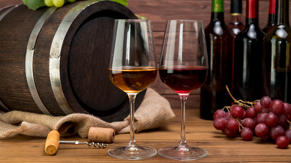 Zwei Weinglässer mit Holzfass und Flaschen im Hintergrund