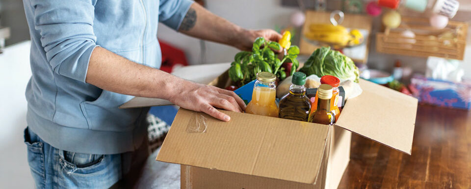 Ein Mann der verschiedene Lebensmittel aus einem Pappkarton herrausholt