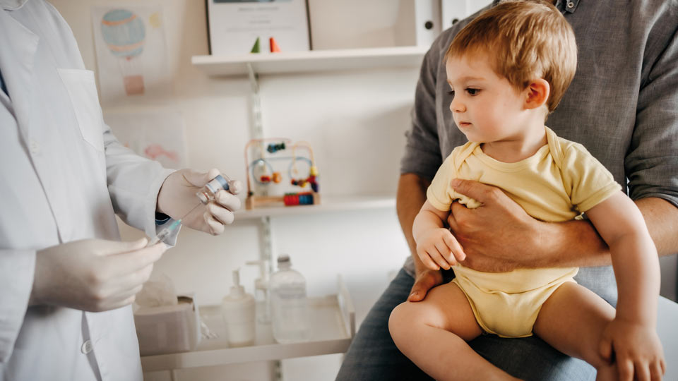 Kleinkind mit Elternteil beim Arzt zum Impfen