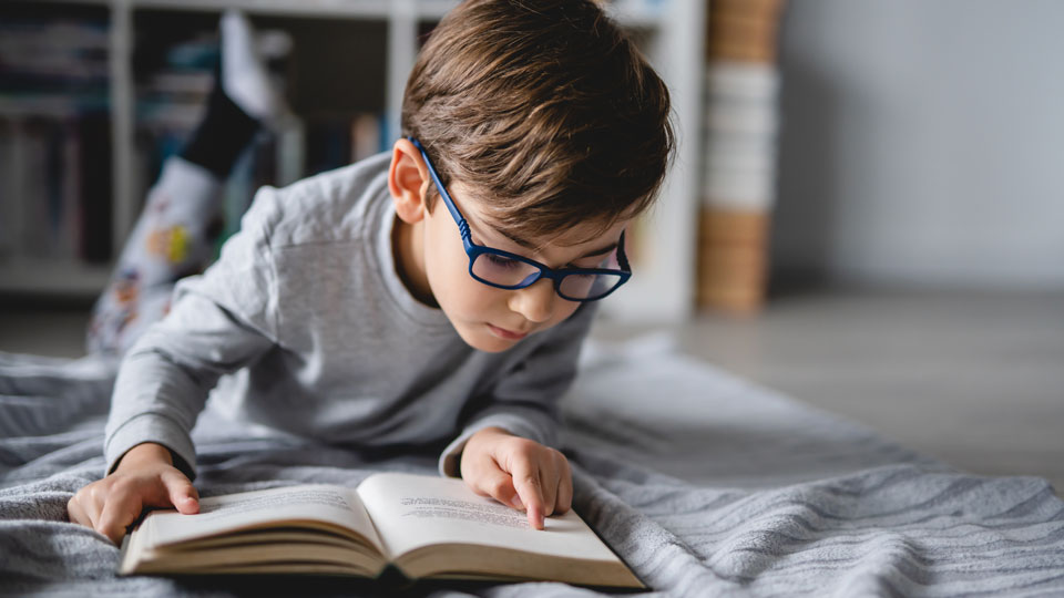 Junge im grauen T-Shirt und Brille liest ein Buch