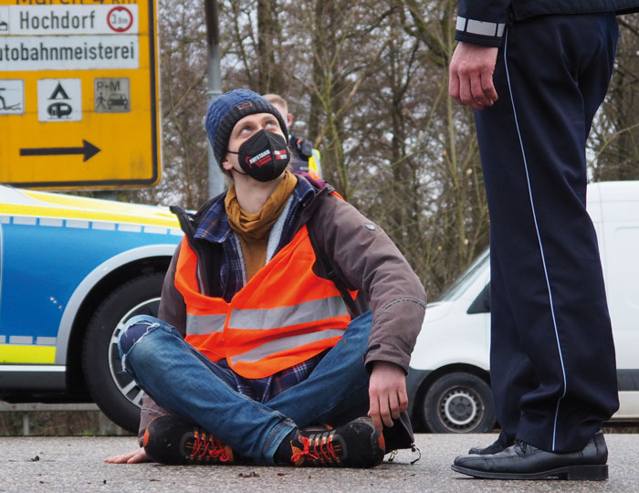 Aktivist sitzend auf dem Boden und einem Polizisten zugewandt
