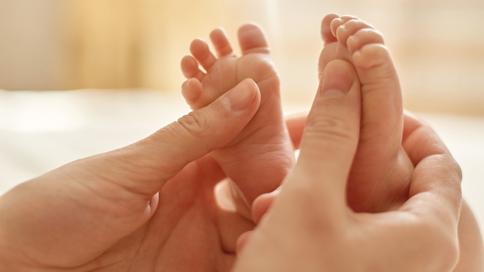 Die Hände einer Mutter die die Füße ihres Neugeborenen in den Händen hält