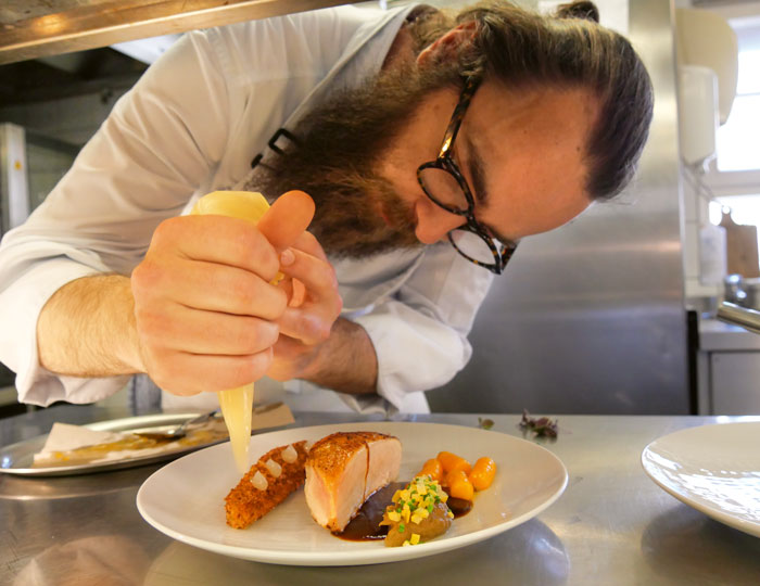 Ein Bild wie Pierre Barrel in seiner Küche das Essen auf dem Teller anrichtet.